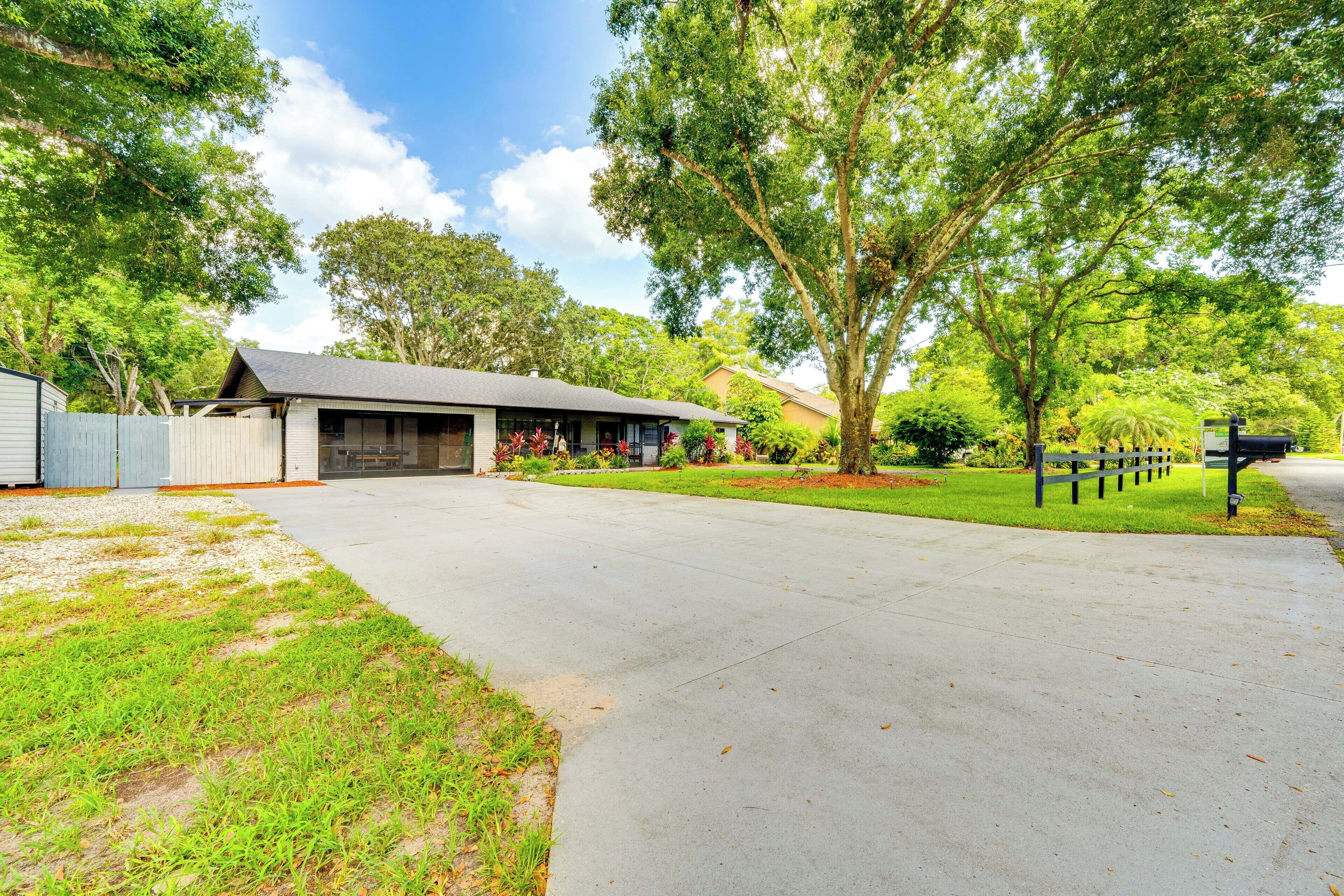 A residential driveway leading to a house with a garage, surrounded by lush greenery and trees.