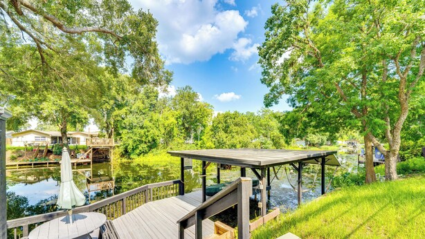 A wooden deck with a table and chairs, overlooking a pond and surrounded by lush greenery. - Spacious Tavares Home w/ Private Outdoor Oasis! (Tavares)