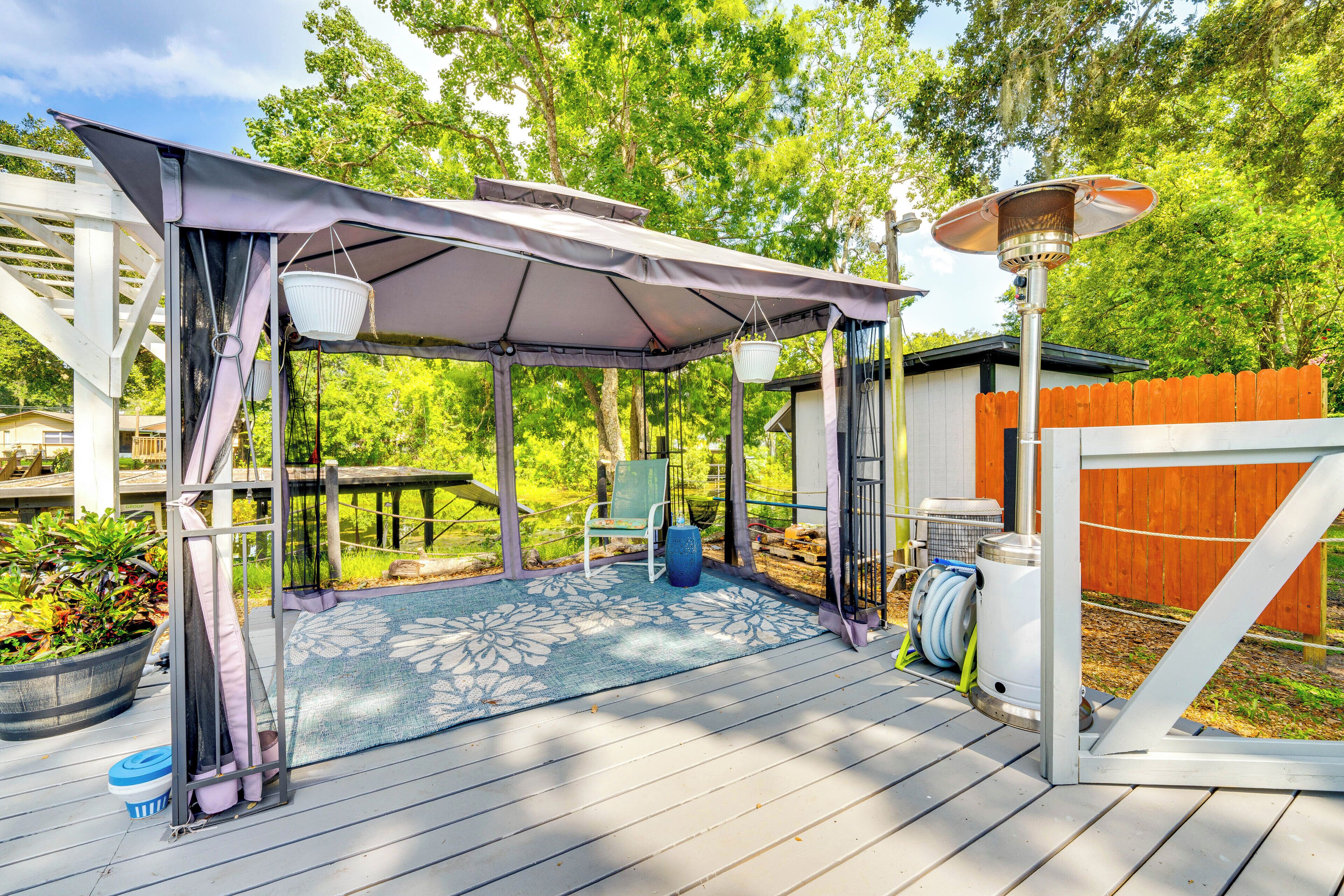 A covered outdoor patio with a table and chairs, surrounded by a wooden deck and a wooden fence.
