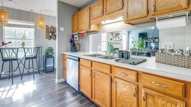 A modern kitchen with wooden cabinets, a dishwasher, and a dining area with a table and chairs. - Knoxville Home w/ Sunroom ~ 9 Mi to Downtown! (Knoxville)