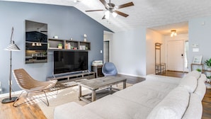 A modern living room with a large sofa, a coffee table, a television, and a ceiling fan. - Knoxville Home w/ Sunroom ~ 9 Mi to Downtown! (Knoxville)