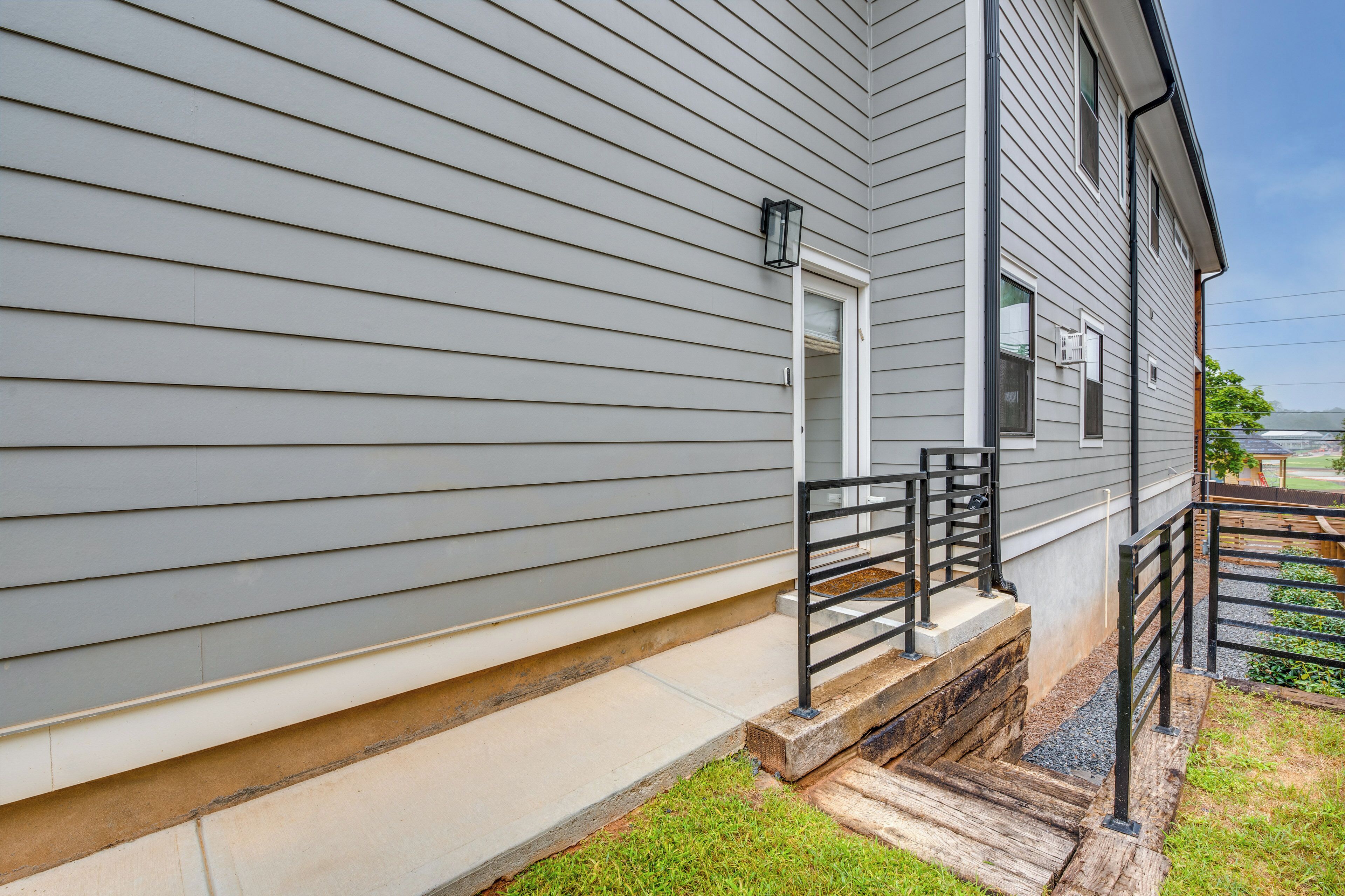 A house with a grey siding exterior, a front porch with a black railing, and a small front yard with grass and a wooden deck.