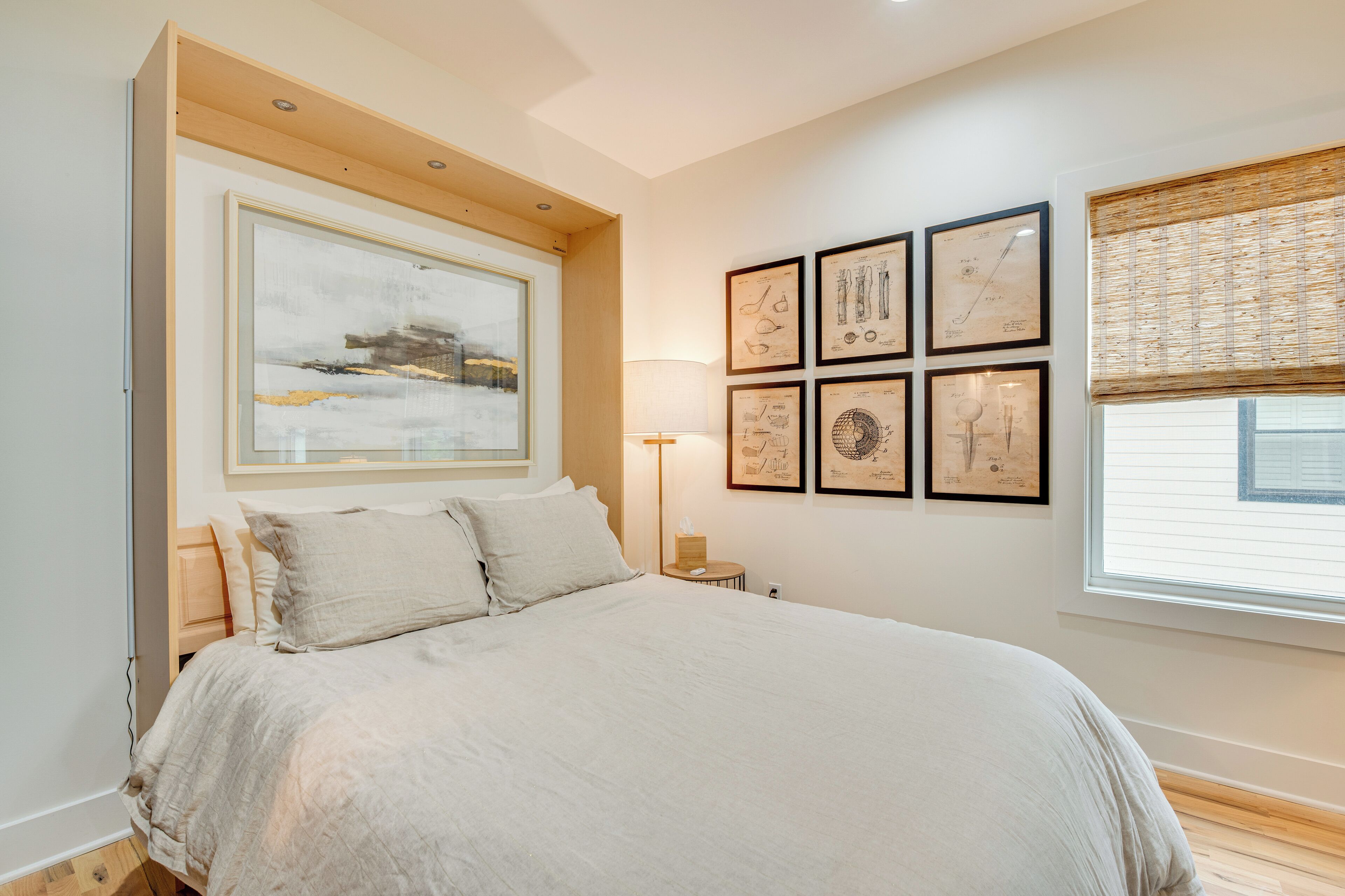A bedroom with a large bed, a nightstand, a wall-mounted lamp, and framed scientific illustrations.