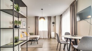 A modern living room with a sofa, dining table, chairs, a TV, and a bookshelf with plants.