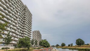 A high-rise residential building with balconies, a river, and trees.