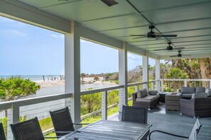 Un espace extérieur abrité, aménagé avec des meubles en osier, une table et offrant une vue sur la plage et l’océan.