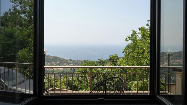A balcony with a view of the sea, a chair, and a railing.