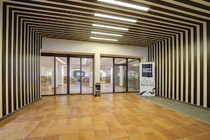 A modern hotel lobby with a geometric patterned ceiling, a tiled floor, and a glass door entrance. - The Loft By FHM (Aqaba)