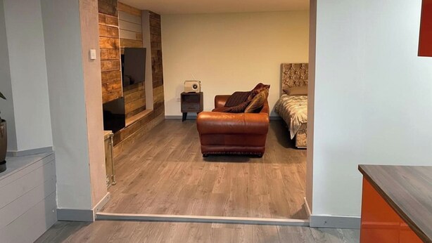 Un salon moderne avec un canapé en cuir marron, un téléviseur fixé à un mur en bois et une petite table d’appoint sur laquelle se trouve une radio.