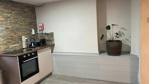 Une cuisine compacte avec un crédence en pierre, un four encastré, un évier et une plante en pot.