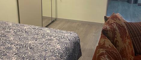 A bedroom with a bed, a wardrobe, a sofa, and a view of a balcony.