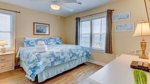 Ein Schlafzimmer mit Bett, Deckenventilator, Schreibtisch und einem Fenster mit Vorhängen.