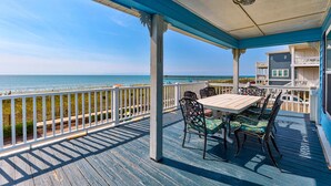 Eine überdachte Terrasse mit Tisch und Stühlen mit Blick auf Strand und Meer.