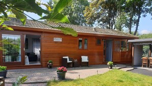 A wooden cabin with a patio area, a covered outdoor seating area, and a small garden with potted plants. - Holiday Home in Garderen by Veluwe (Garderen)