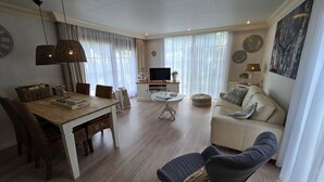 A modern living room with a wooden dining table, a sofa, and a TV. - Holiday Home in Garderen by Veluwe (Garderen)