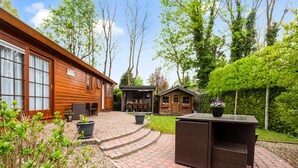 A wooden cabin with a patio area, outdoor furniture, and a small shed. - Holiday Home in Garderen by Veluwe (Garderen)
