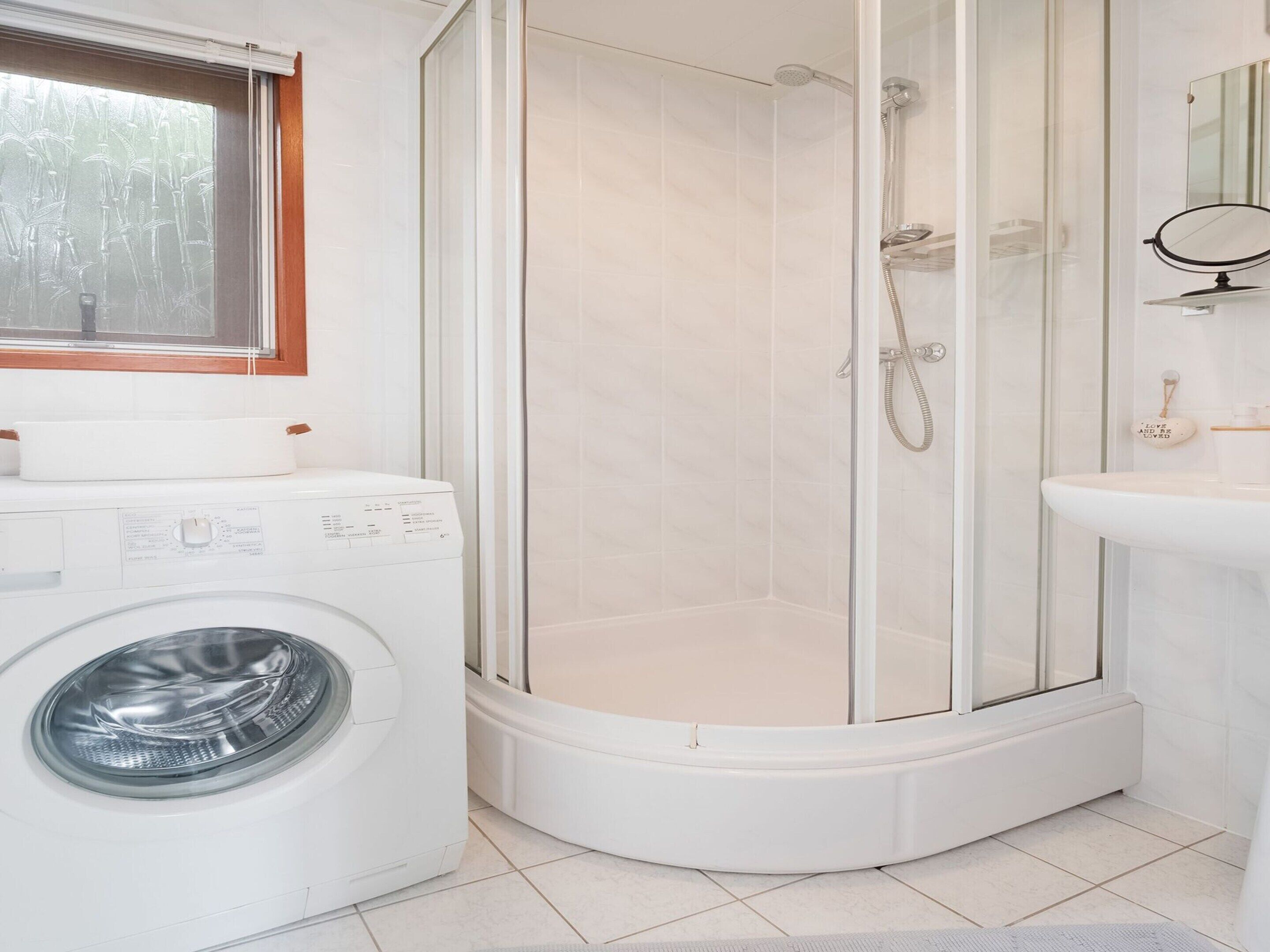 A modern bathroom with a glass-enclosed shower, a washing machine, and a sink with a mirror.