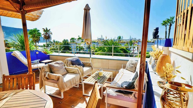 A terrace with a view of the sea, furnished with chairs and a table, and a decorative lantern. - Casa Vivienne: Puerto de Mogan Beach, Gran Canaria (Peurto De Mogan)