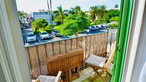 A balcony with a wooden table and chairs, overlooking a street with parked cars and palm trees. - Casa Vivienne: Puerto de Mogan Beach, Gran Canaria (Peurto De Mogan)
