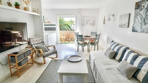 A modern living room with a TV, sofa, and dining area. - Casa Vivienne: Puerto de Mogan Beach, Gran Canaria (Peurto De Mogan)
