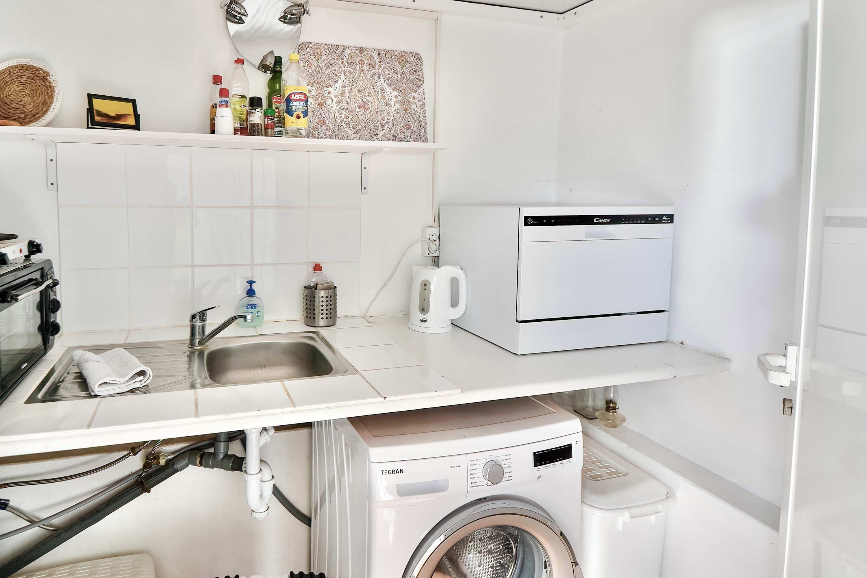 A compact kitchen with a washing machine, a coffee maker, and a sink.