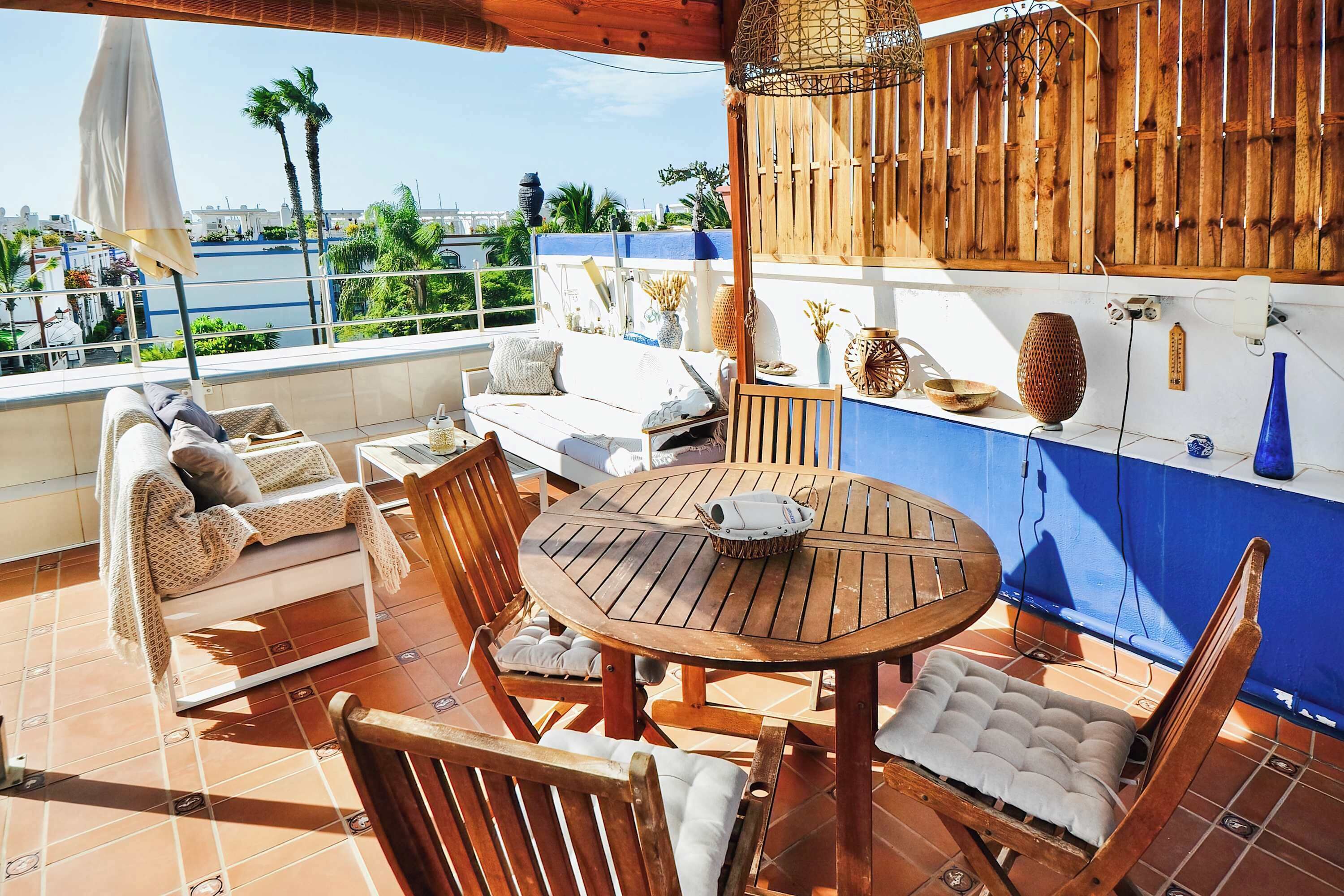 A terrace with a wooden table and chairs, a white sofa, and a view of the sea.