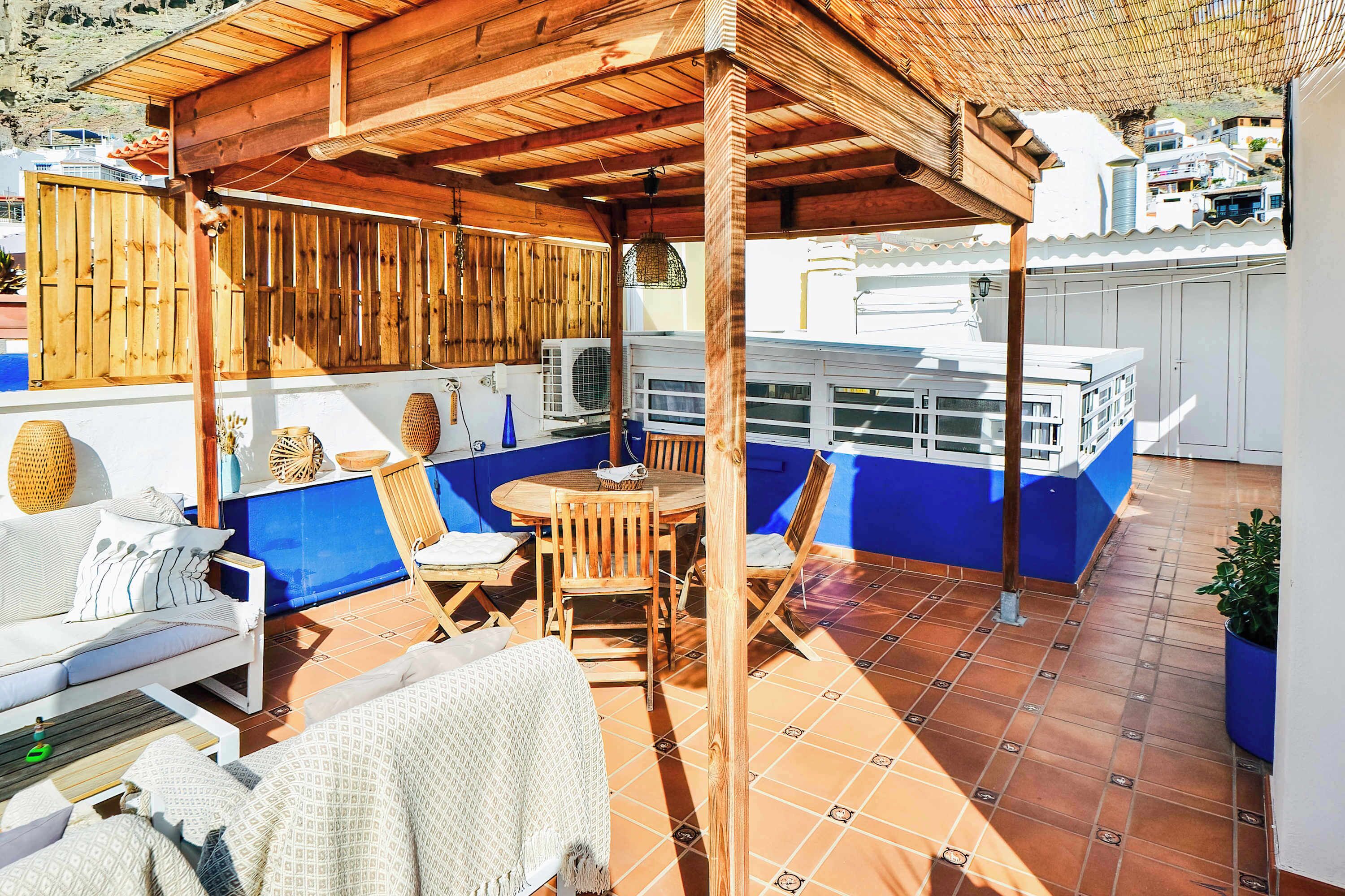 A covered outdoor seating area with a wooden pergola, a blue and white bar area, and a tiled floor.