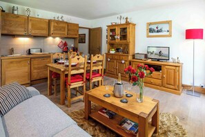 Una sala acogedora con una mesa de comedor de madera dispuesta para dos personas, un sofá y una cocina con armarios de madera y una lámpara roja.
