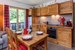 Een gezellige keuken met houten kastjes, een eettafel gedekt voor twee personen en uitzicht op het groen door een schuifdeur.