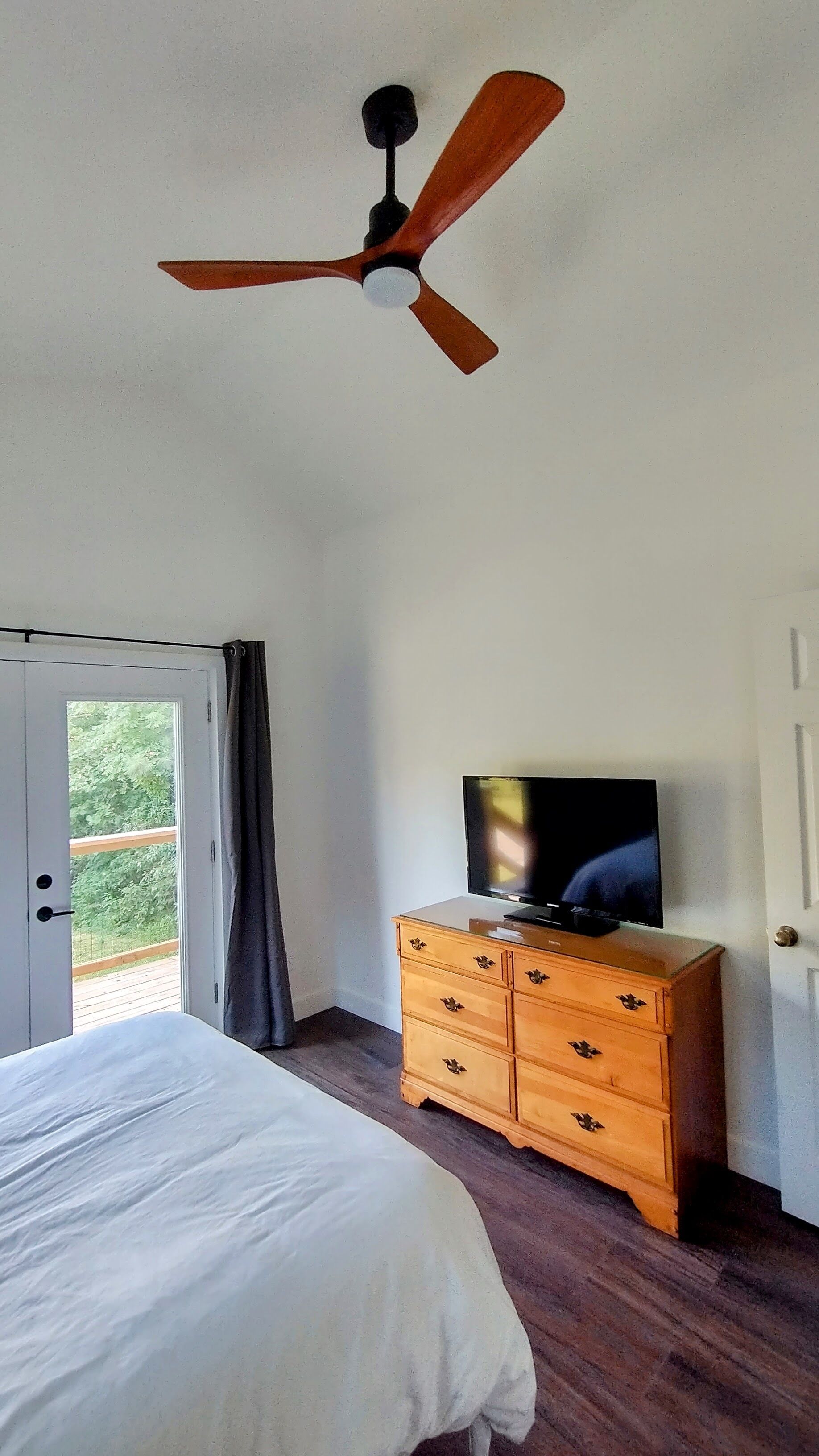 Een slaapkamer met een bed, een houten dressoir, een plafondventilator en een televisie.