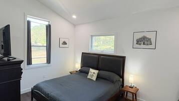 Une chambre à coucher comprenant un lit, un ventilateur de plafond, une table de chevet avec une lampe, une commode et deux fenêtres.