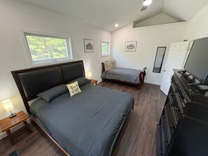 Ein Schlafzimmer mit einem großen Bett, einem kleineren Bett, einem Fernseher und einer Kommode.