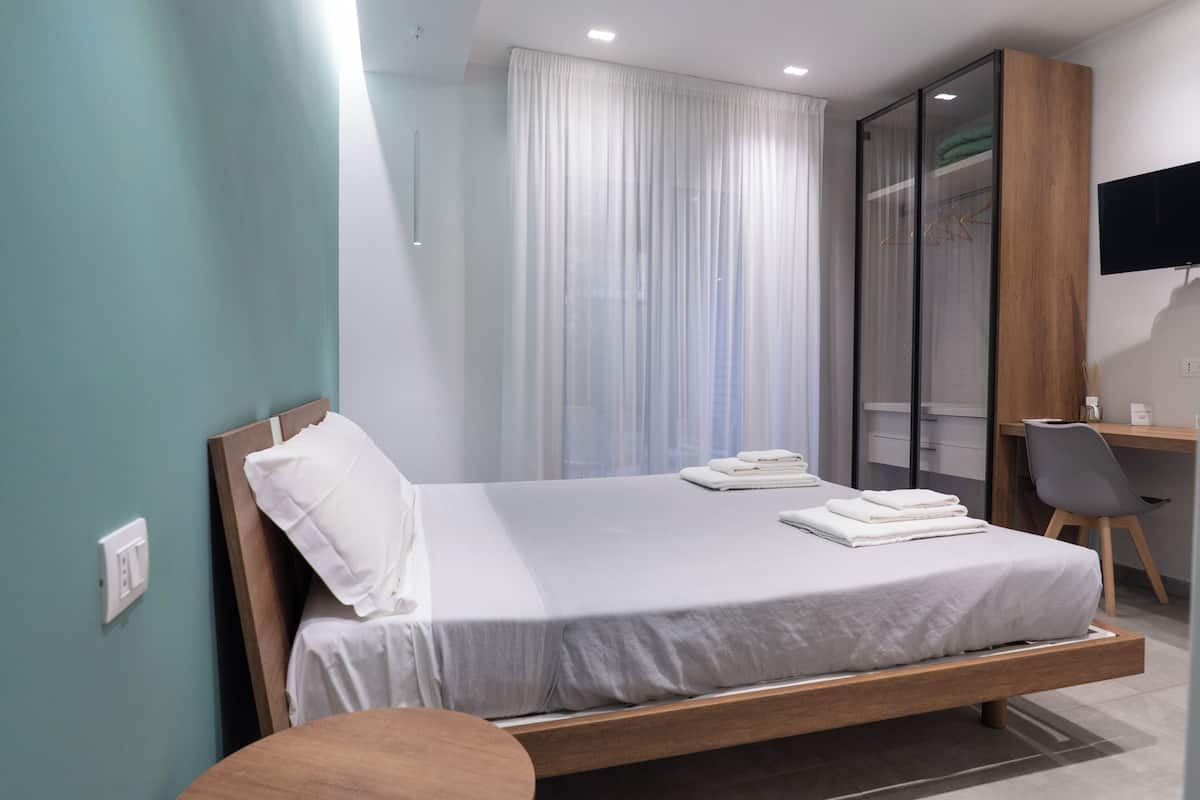 A modern hotel room with a single bed, a desk, and a chair.