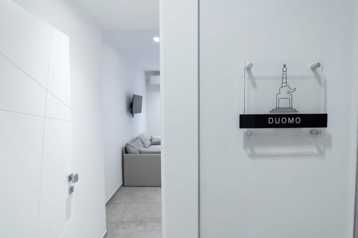 A modern hotel corridor with a clear sign reading "DUOMO" and a minimalist statue decoration.