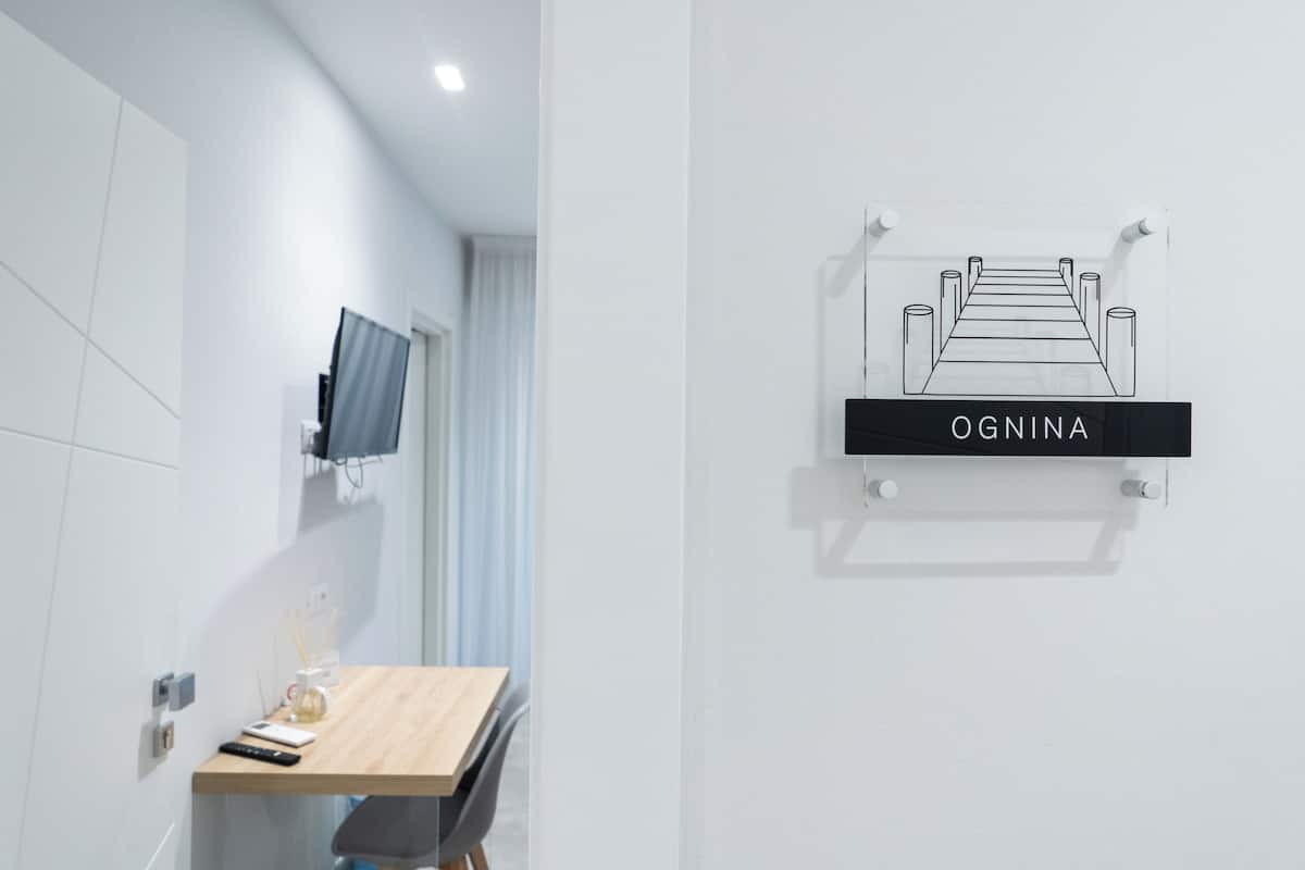 A modern hotel room with a wooden desk, a mounted television, and a wall-mounted sign reading 'OGNINA'.