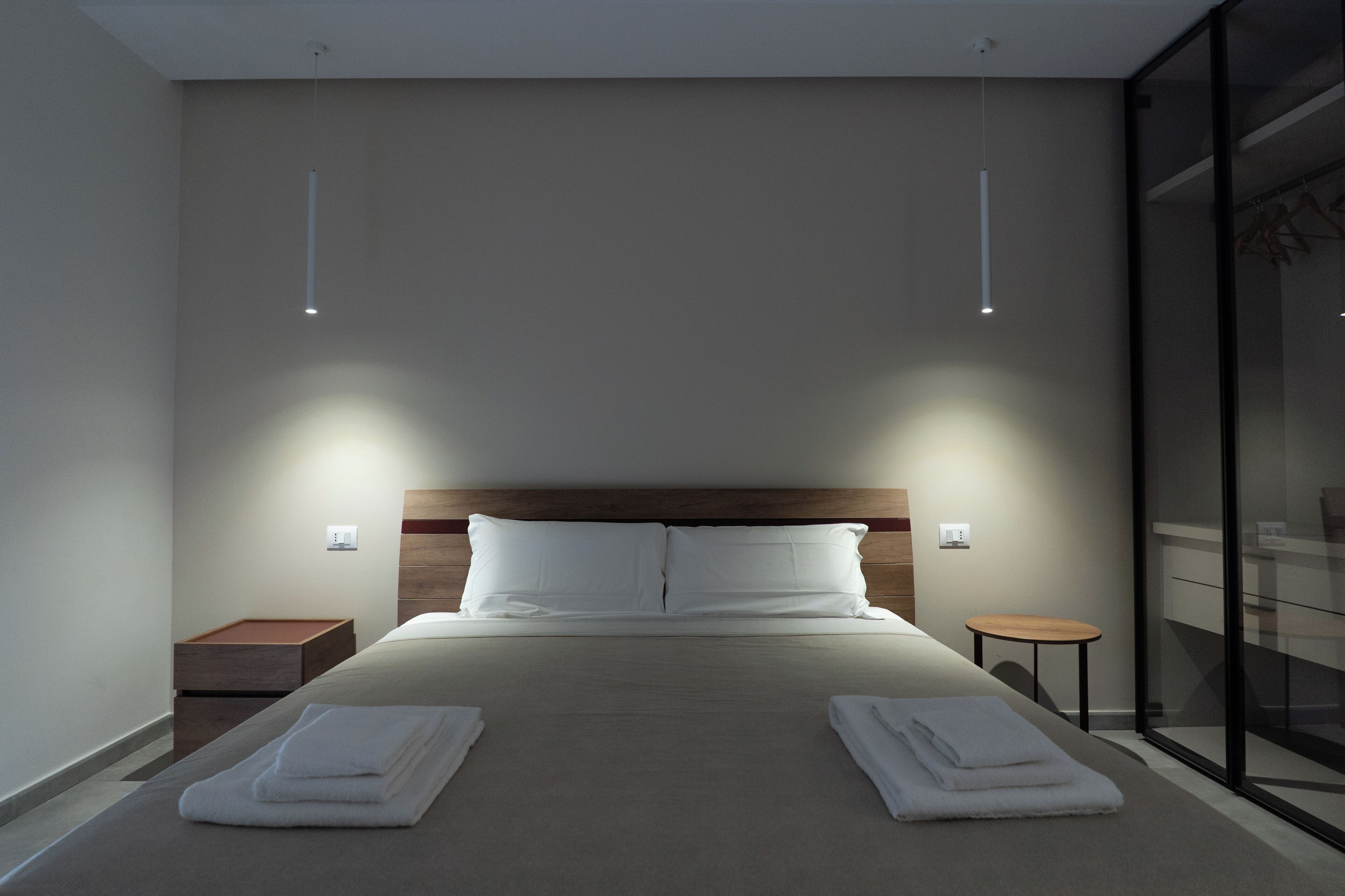 A modern hotel room with a large bed, two bedside tables, and a glass partition.