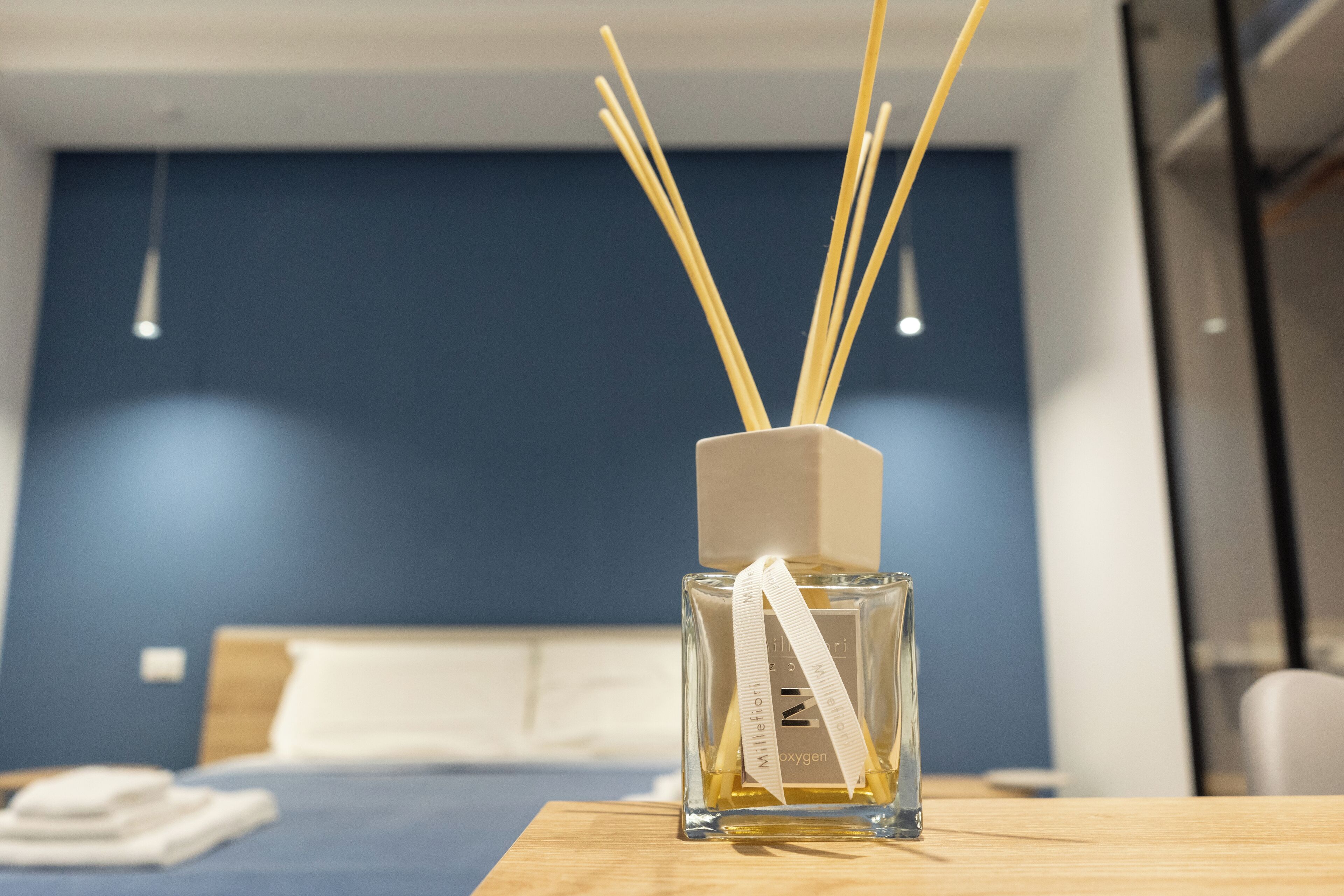 A clear glass bottle with a white label and reed sticks on a wooden table in a hotel room.