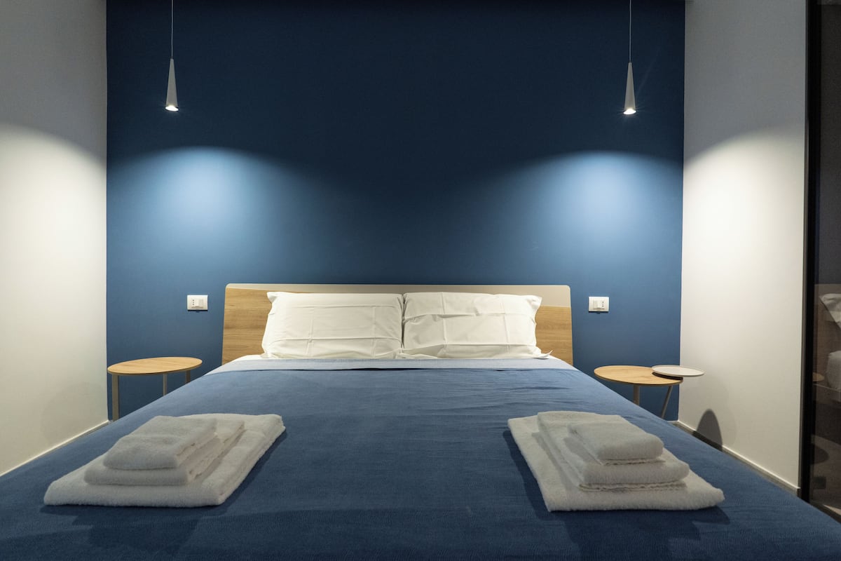 A neatly made bed with white linens, two bedside tables, and pendant lights.