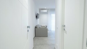 A modern, minimalist hallway with a grey sofa and a mounted TV. - CATANIA E DINTORNI LIVING ROOMS (Catania)