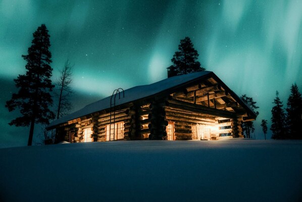 Una cabaña de troncos con techo nevado, paredes de madera y una ventana con una escalera.