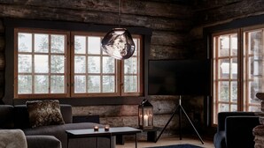 Interior acogedor de una cabaña de troncos con un sofá, una mesa de centro, una lámpara de pie y un televisor.