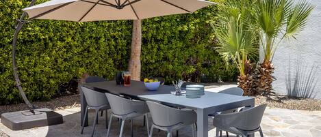 An outdoor patio with a table, chairs, an umbrella, and a stone floor.