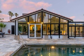Una casa moderna con piscina, amplios ventanales de vidrio y un patio de piedra.