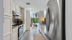 Une cuisine moderne dotée d’appareils électroménagers en acier inoxydable, de meubles blancs et offrant une vue sur un espace extérieur aménagé pour se détendre.
