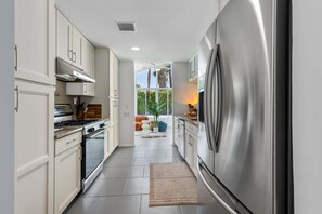 A modern kitchen with stainless steel appliances, white cabinetry, and a view to an outdoor seating area.