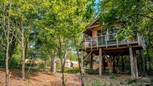 Una casa del árbol de madera con balcón, rodeada de frondosa vegetación verde.