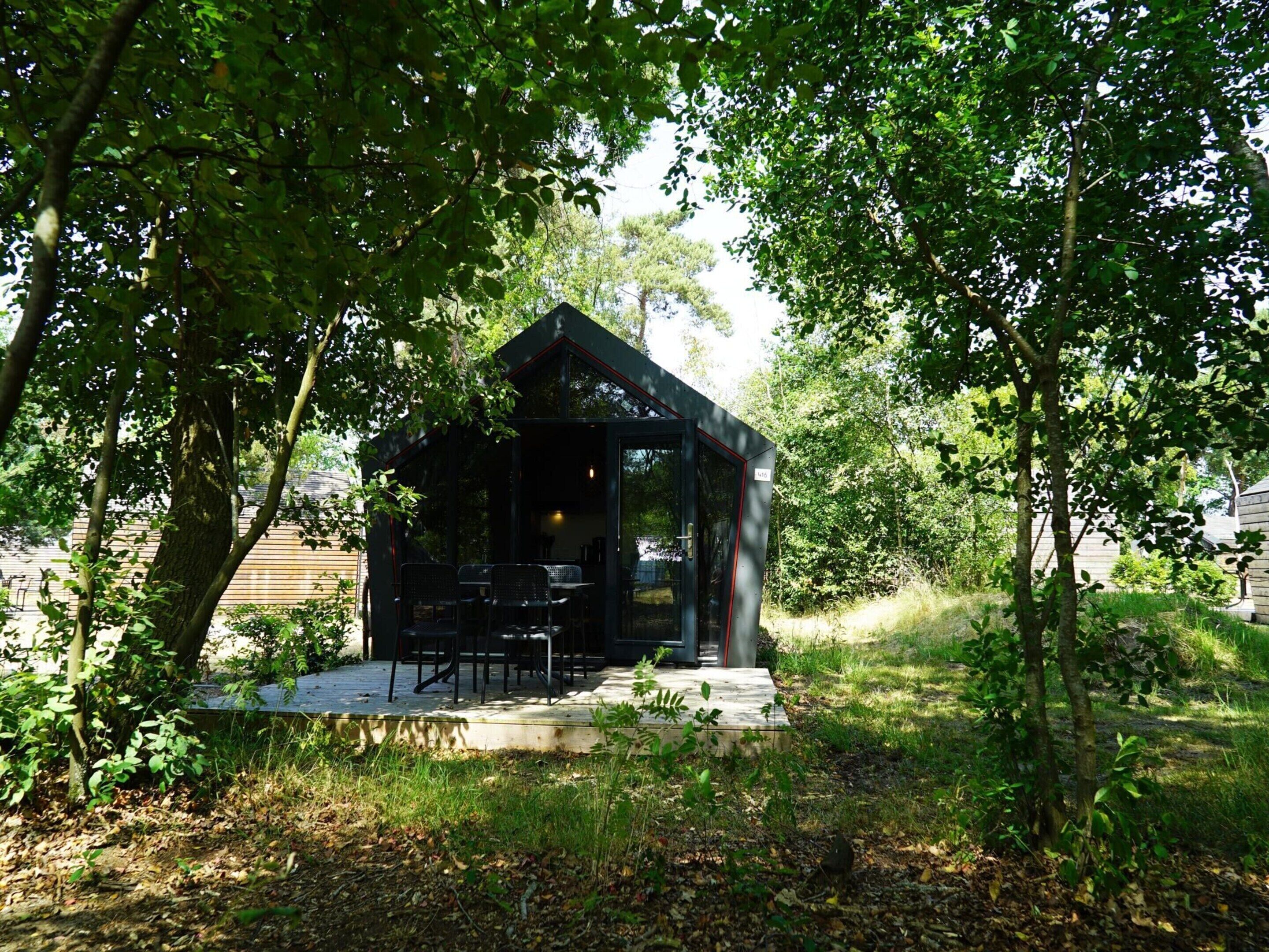 A small, modern outdoor structure with a glass enclosure, surrounded by trees and a wooden deck.