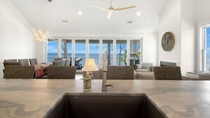 A modern living room with a large window, a ceiling fan, and a dining area with a sink. - Plage d'Amour "Beach of Love" (Port Saint Joe)