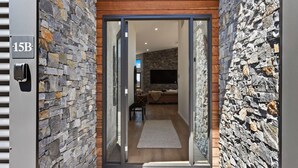 Una entrada moderna con paredes de piedra, suelo de madera y un piso de vidrio corredera que da a una sala de estar con un sofá y televisor de pantalla plana.