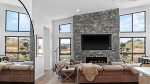 Una sala de estar moderna con chimenea de piedra, ventanas amplias y un espacio de asientos acogedor.